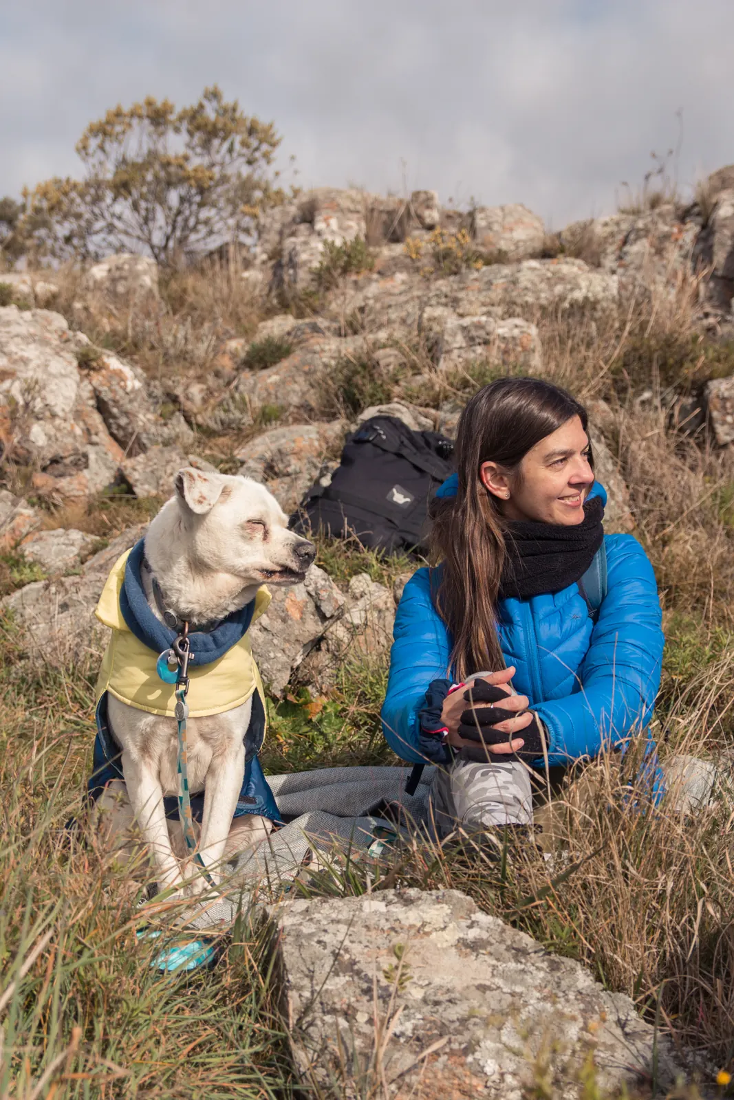 Mujer descansando junto a su perro entre las piedras